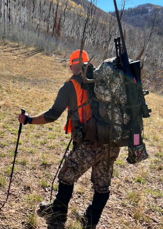 A hunter carrying a pack along a wooded mountain trail